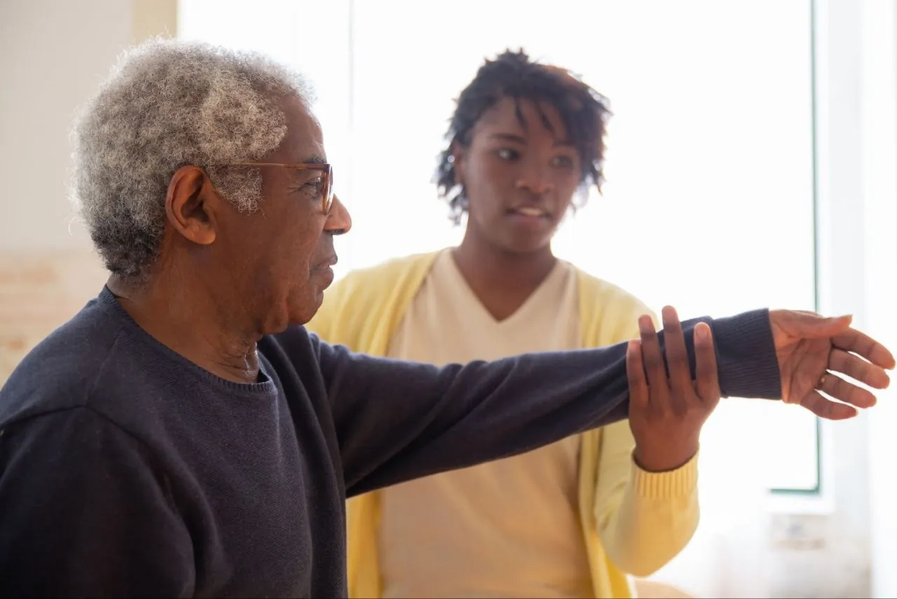 A therapist guiding an older man through an arm exercise