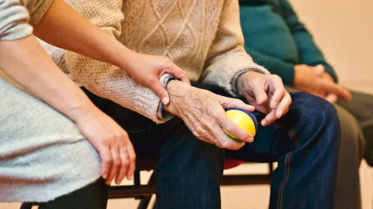 A therapist helping an older patient squeeze a grip ball