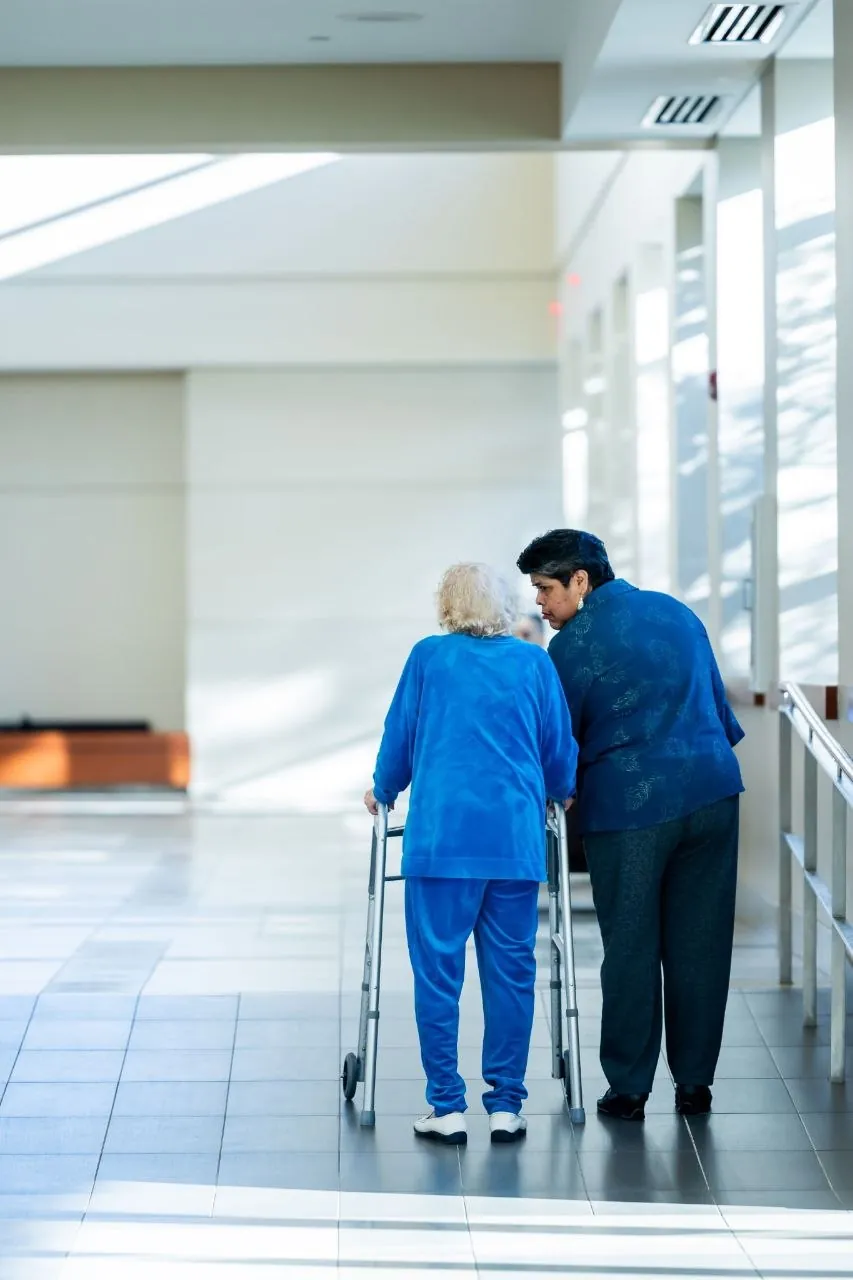 A caregiver walking beside an older woman using a walker